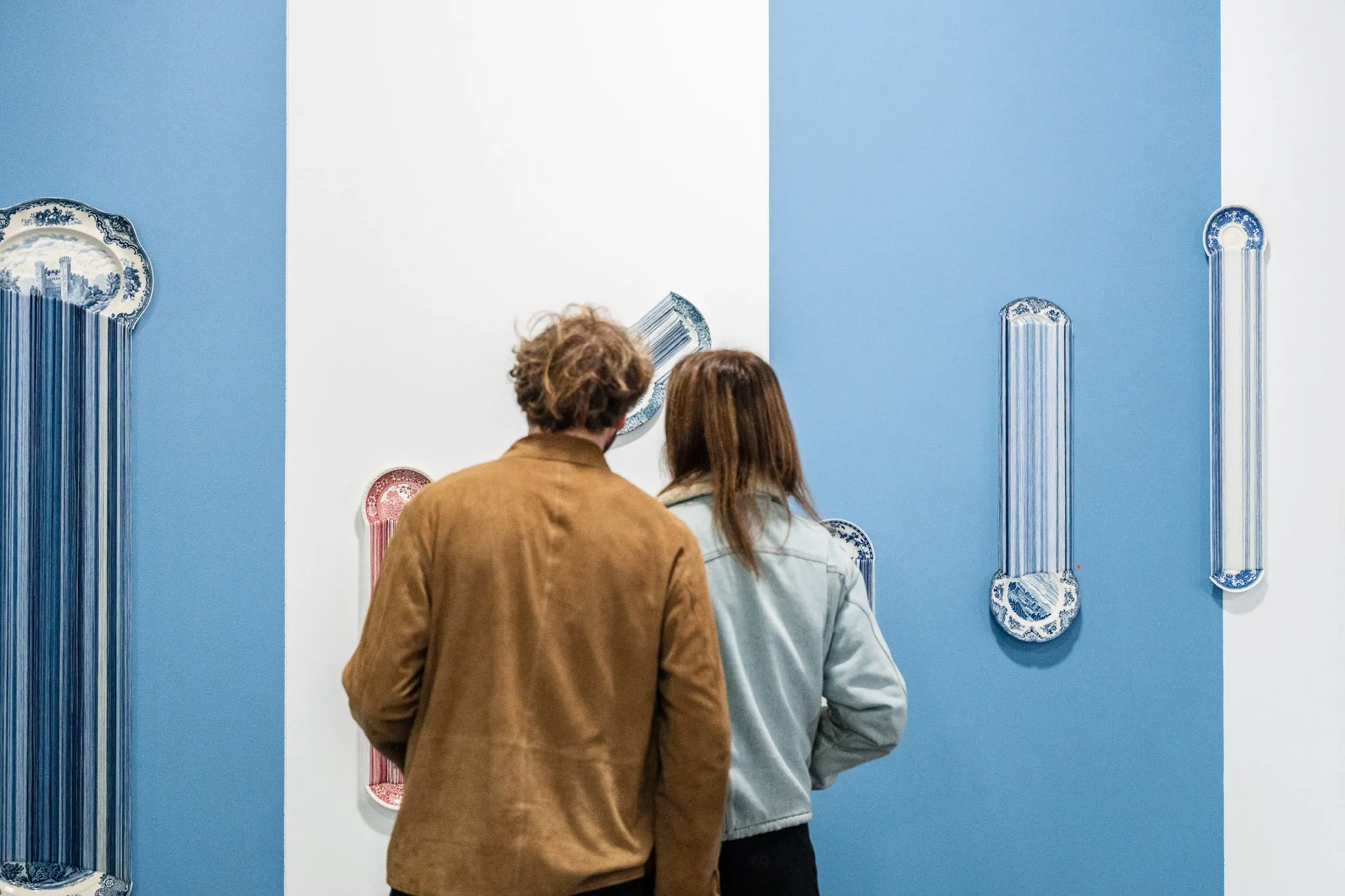 Two visitors in front of blue and white plates stretched into long drips down a blue wall.