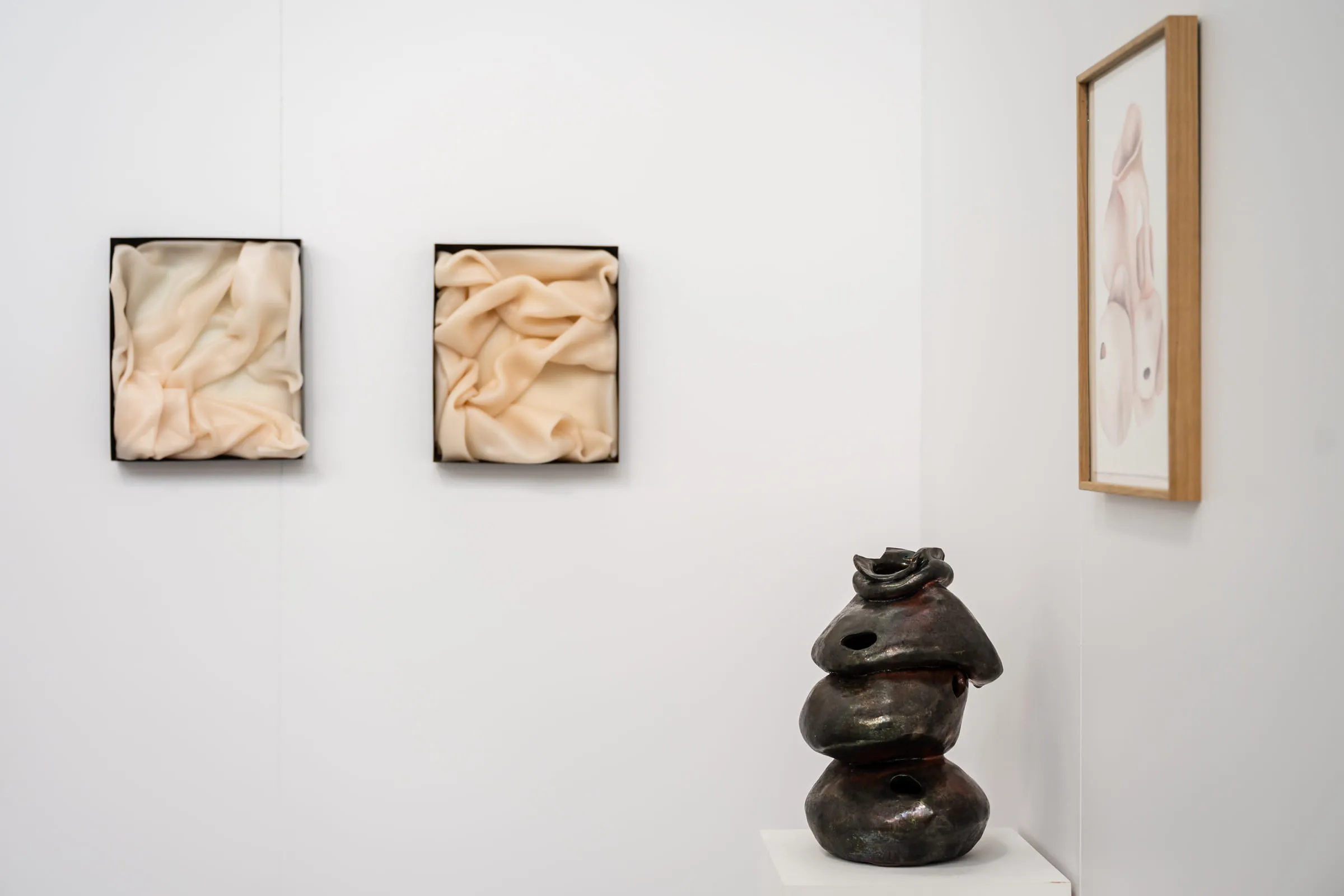Two pale framed reliefs on the wall beside a dark ceramic sculpture of stacked volumes.