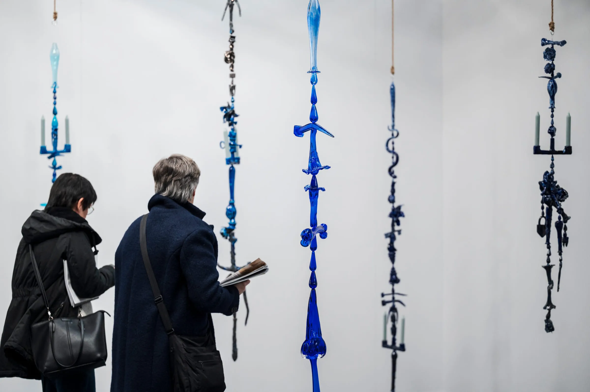 Two visitors in front of long hangings of blue glass on the wall.