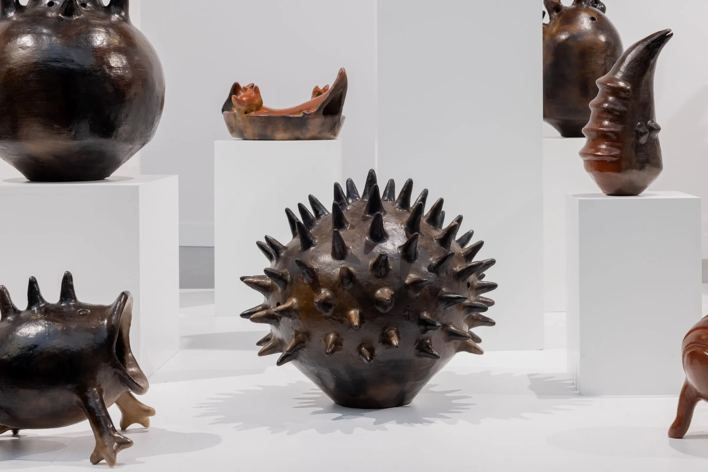 Dark ceramic vessels on white plinths, one of them covered in spikes.