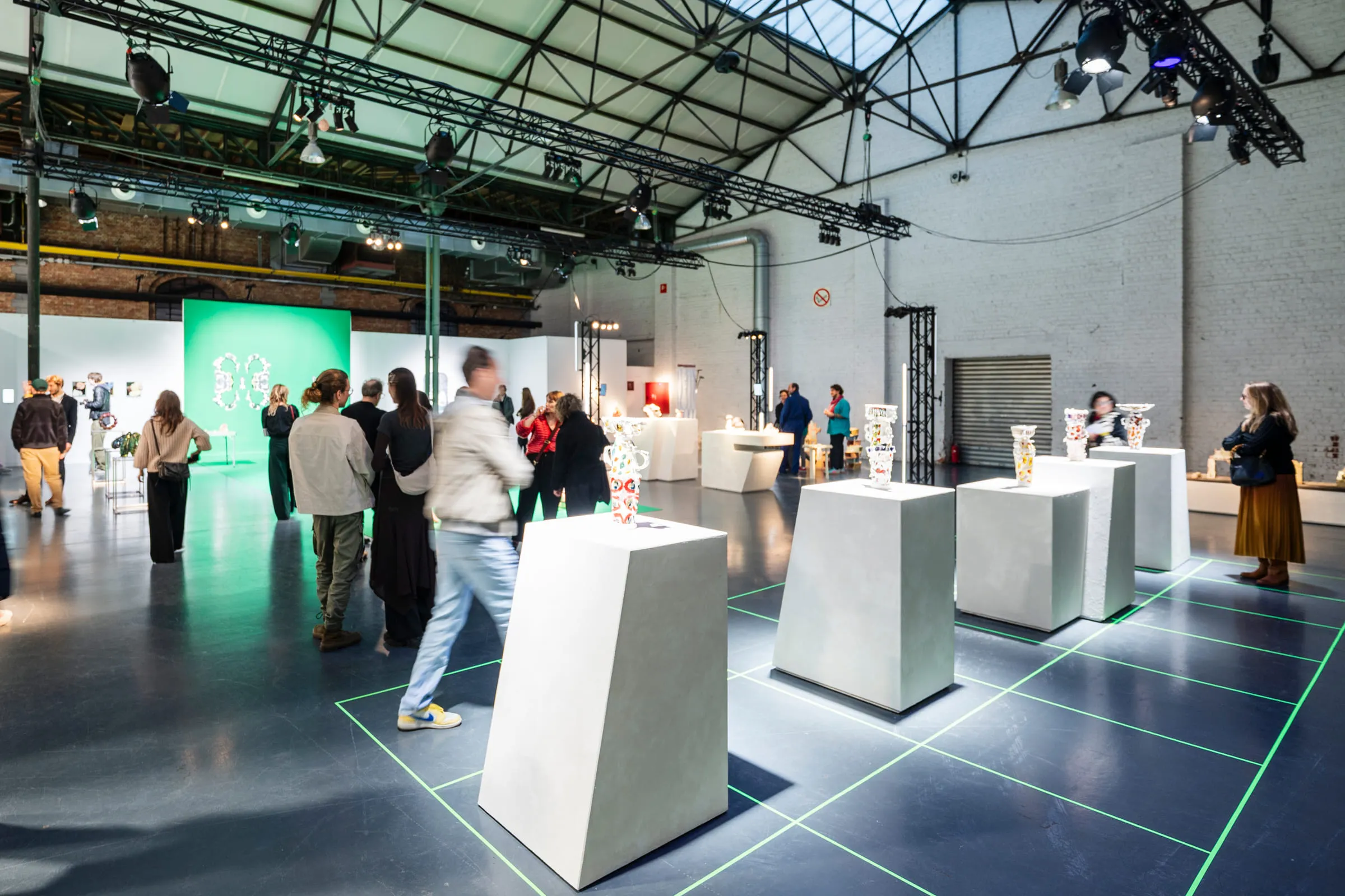 White plinths carrying ceramic pieces in a hall, lines of green light drawn across the floor.